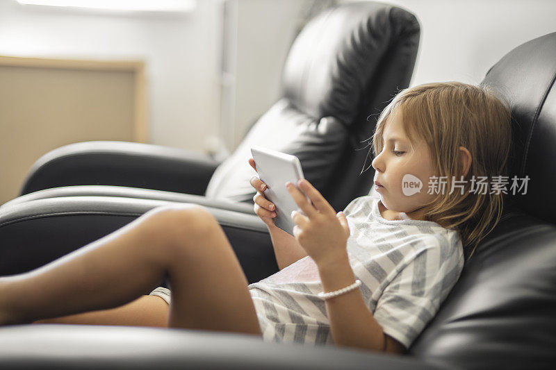 担心的小女孩穿着睡衣，坐在扶手椅上，在家里使用数码平板电脑