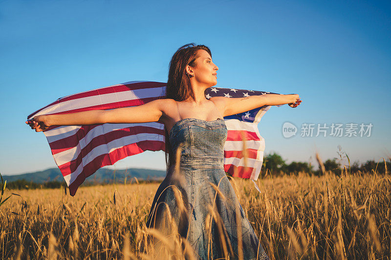 拿着美国国旗的妇女站在麦田里