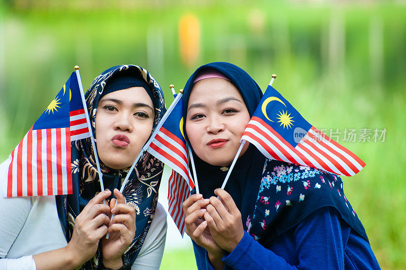 两名年轻的马来西亚妇女戴着头巾，挥舞着马来西亚国旗，以崇高的爱国主义精神庆祝独立日