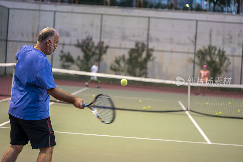 教练正正手击球，让网球选手集中精力在硬地球场的前景上