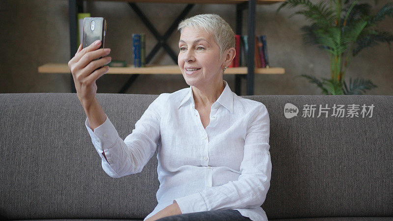 上了年纪的成功商业女性坐在沙发上用智能手机进行视频通话