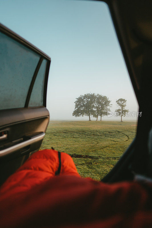 睡袋里的男人在车里醒来。草原日出