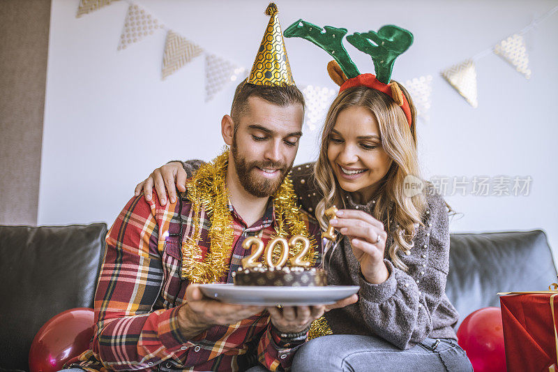 年轻的朋友们在家庆祝圣诞节，拿着巧克力蛋糕，上面点燃了2021年的数字蜡烛