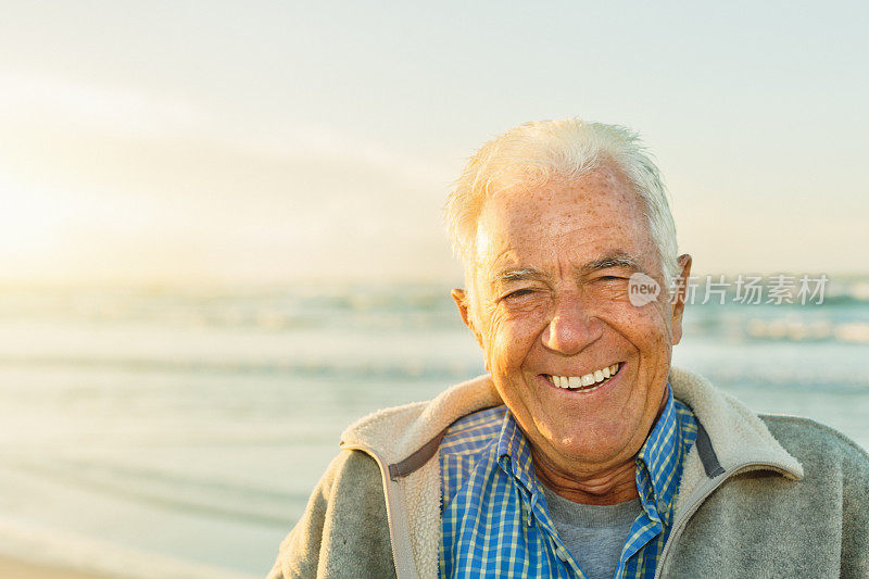 在田园诗般的大海边，一位白发老人对着镜头开心地笑