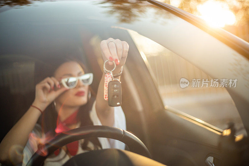 一个漂亮的女人坐在车里，手里拿着一把车钥匙。新司机。一个年轻的女人正在展示汽车钥匙。