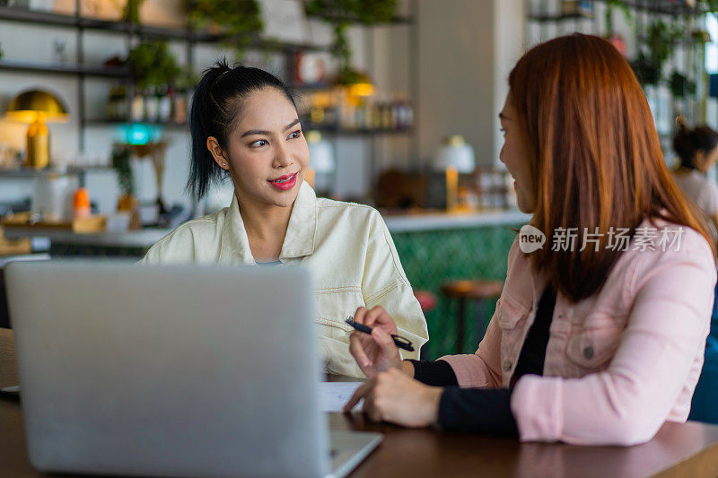 两个千禧亚洲混血女性在共同工作空间讨论工作。