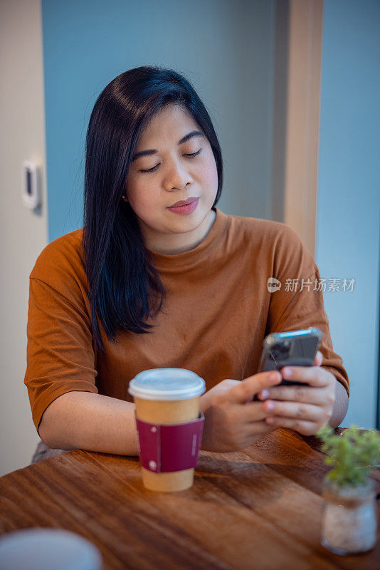 一名女子在自助餐厅的餐桌边喝咖啡休息时用智能手机发短信