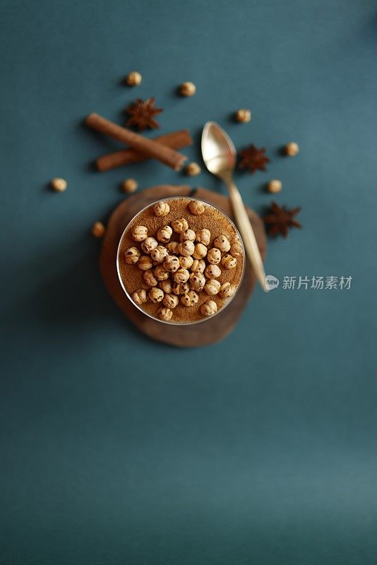 传统土耳其甜点“Boza”，装在玻璃杯里，木制的杯垫上，背景为蓝绿色