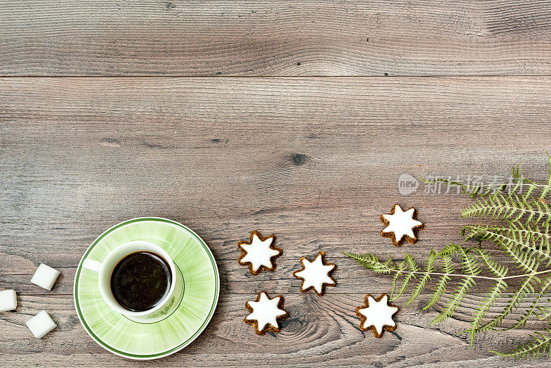 绿色陶瓷咖啡杯与浓缩咖啡，绿色蕨叶和肉桂星饼干木制背景