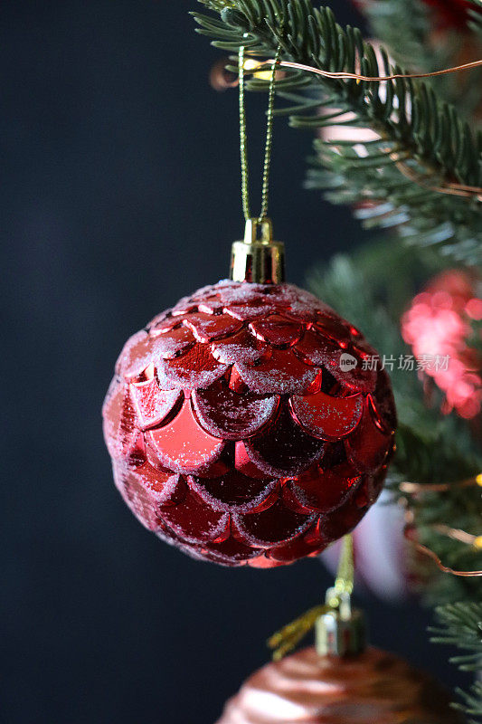 个人的特写图像，红色，有质感的小装饰物挂在人造圣诞树的树枝上，云杉针，模糊的白色童话灯的背景，复制空间
