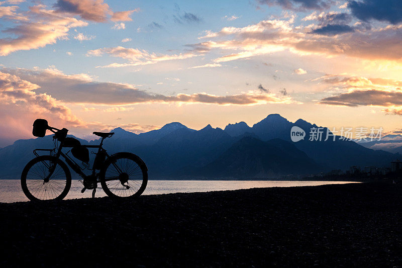 剪影拍摄自行车在海滩，海和山的背景景观