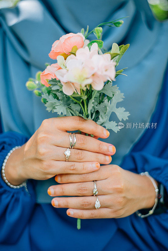 时尚的亚洲女性，手捧一束鲜花，手捧钻石戒指、银手链等奢华配饰