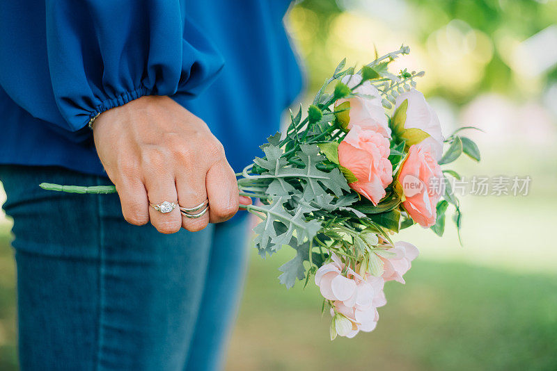戴着钻石戒指、银手链等奢华饰品的时尚女性，手捧一束鲜花在户外。