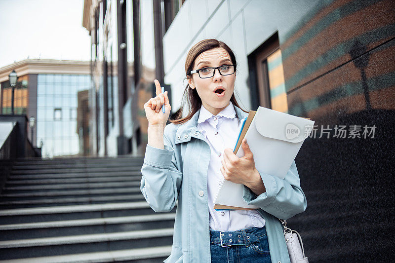 我有个主意。年轻的女商人戴着眼镜，手里拿着一摞文件，在城市里竖起食指。生活方式