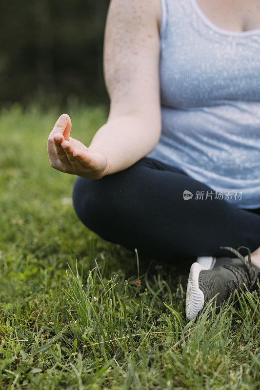 一位匿名的超重女性坐在草地上做瑜伽