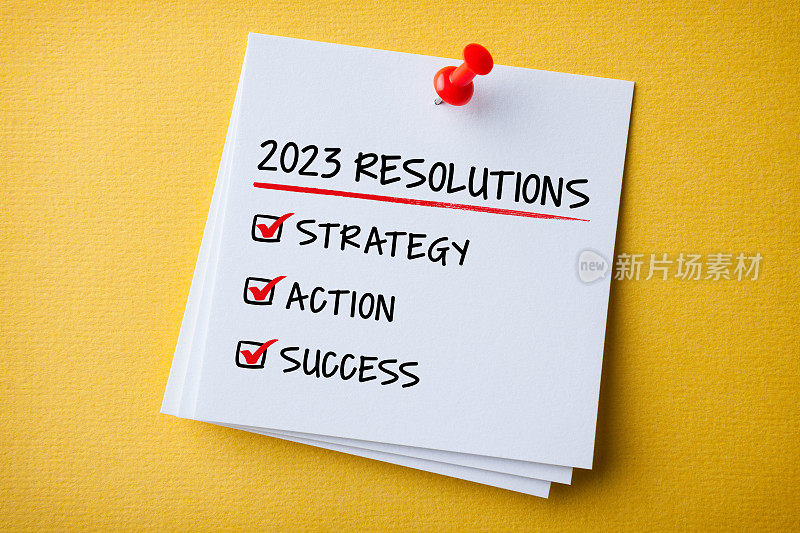 白色便签与2023年新年决心和红色图钉在黄色纸板背景
