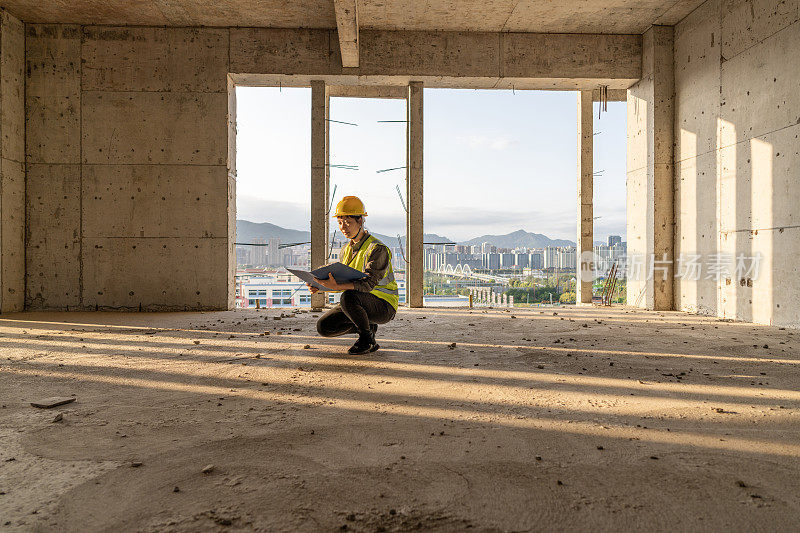 一位亚裔女工程师蹲在建筑工地的地板上看图纸