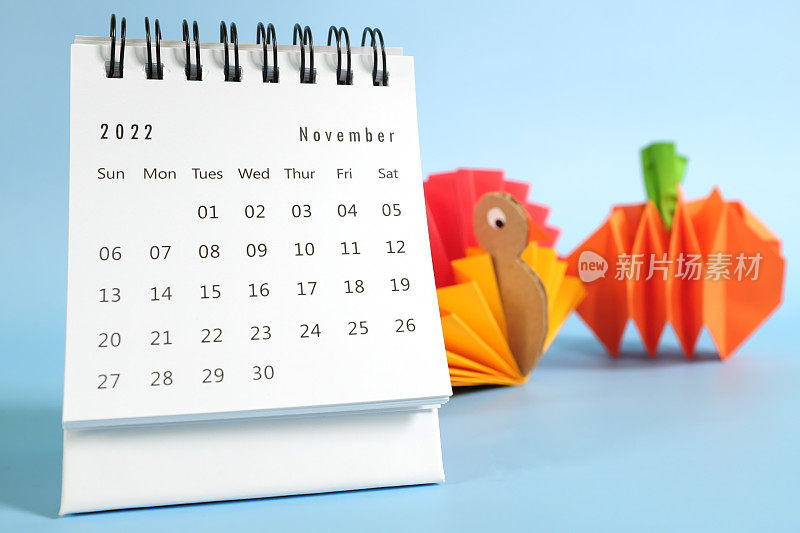你好，2022年11月与感恩节的概念。桌上日历与火鸡和南瓜纸工艺在蓝色背景。