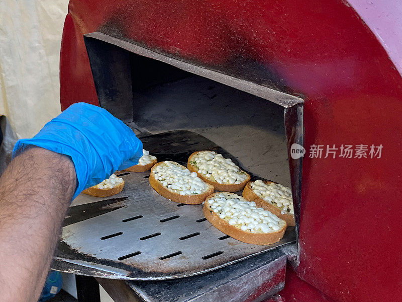 特写的人戴着蓝色，橡胶手套滑迷你披萨到户外，不锈钢，石基披萨烤箱上长柄披萨桨，关注前景