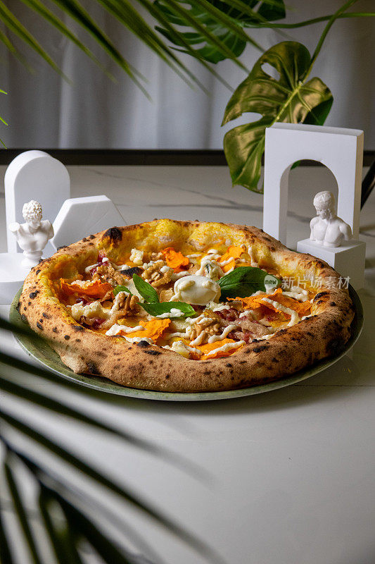 那不勒斯披萨，南瓜和马苏里拉奶酪，大理石桌子上有树叶和雕像