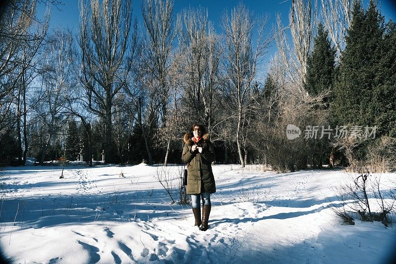 在阳光明媚的冬日公园里，一位开朗成熟的女士正戴着耳机听着音乐