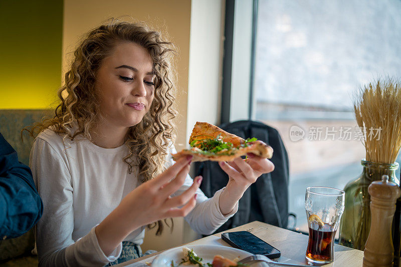 女人正从烧木头的炉子里吃披萨。在意大利餐厅吃午餐。