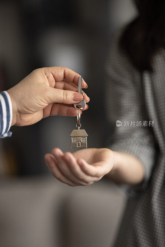 近距离聚焦钥匙，微笑的女子房地产经纪人出售公寓