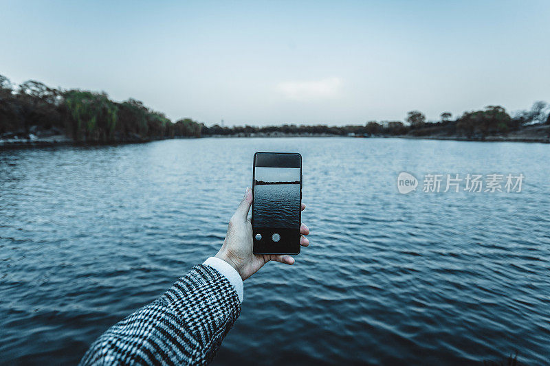 一名男子在户外用手机拍摄日落时分的湖泊