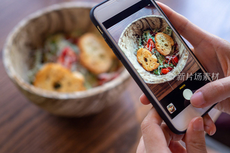 手用手机拍照或拍照的食物。沙拉放在碗里，放在桌子上，看起来很好吃。晚餐的健康食物