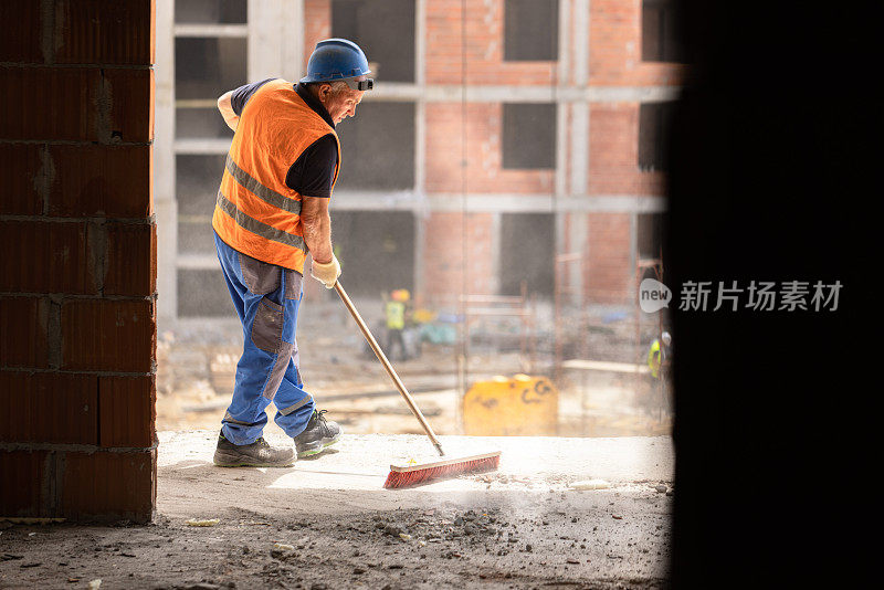 无法辨认的中年建筑工人正在用扫帚清理工地上的灰尘