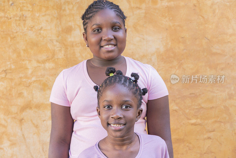 幸福的美国黑人小姐妹在户外墙背景前一起微笑的肖像
