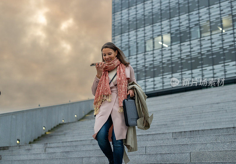 时髦的女商人在办公大楼外用手机发送语音信息