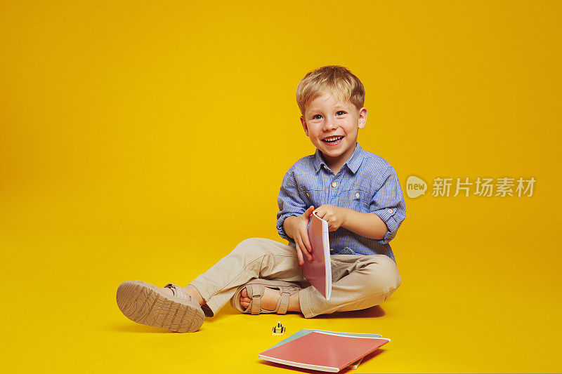 兴奋的男生坐在地板上，拿着笔记本，对着镜头开心地微笑。