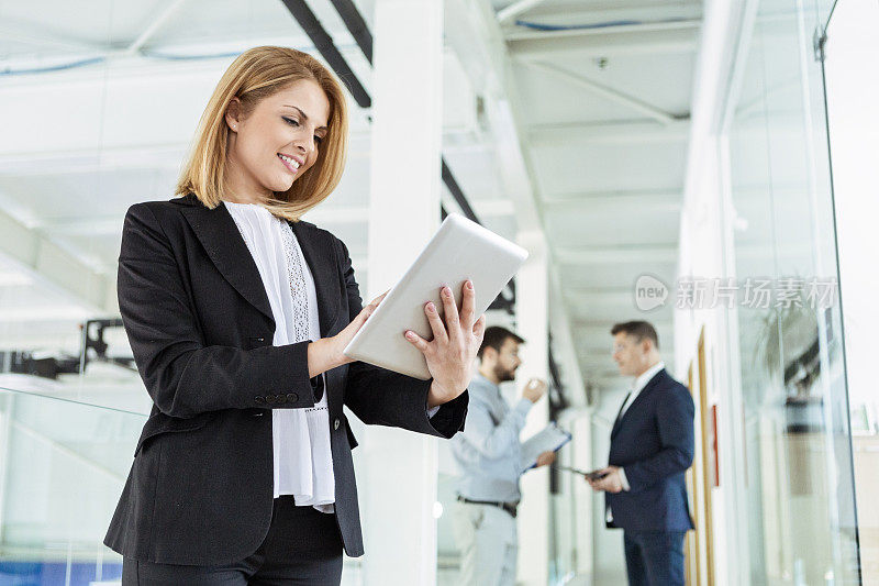 一个女人在办公室里使用她的数码平板电脑，背景是她的同事