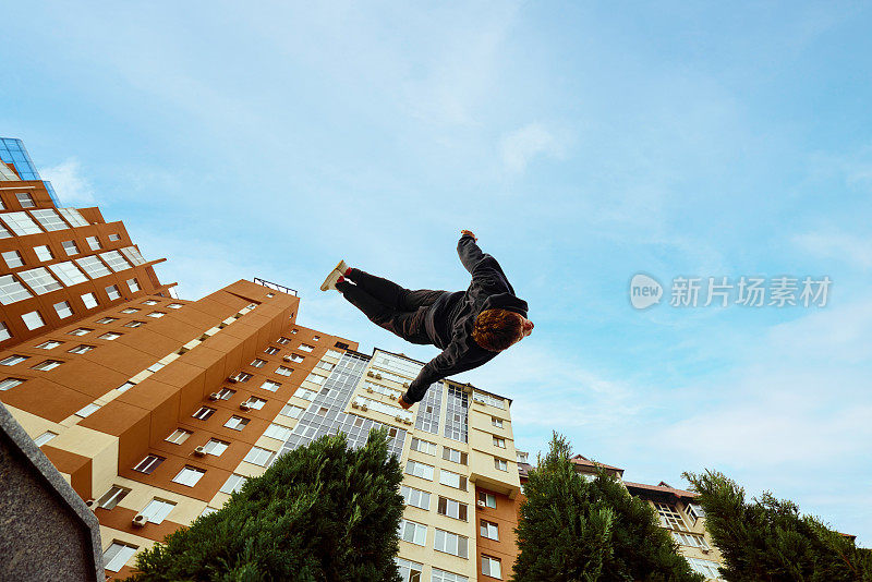 运动员，年轻人跳得很高，在城市上空做后空翻，高层建筑和公园的天空景观。眼鱼滤镜。