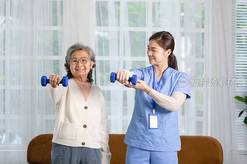亚洲女医生建议老年病人到物理治疗师家里用哑铃锻炼。微笑的护士帮助老年病人锻炼，使肌肉强壮。理疗师护理。