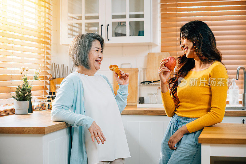 在厨房里，一个迷人的年轻亚洲女人和她的母亲分享了一个团聚的时刻。他们的微笑反映了食物和学习带来的幸福和家庭纽带。