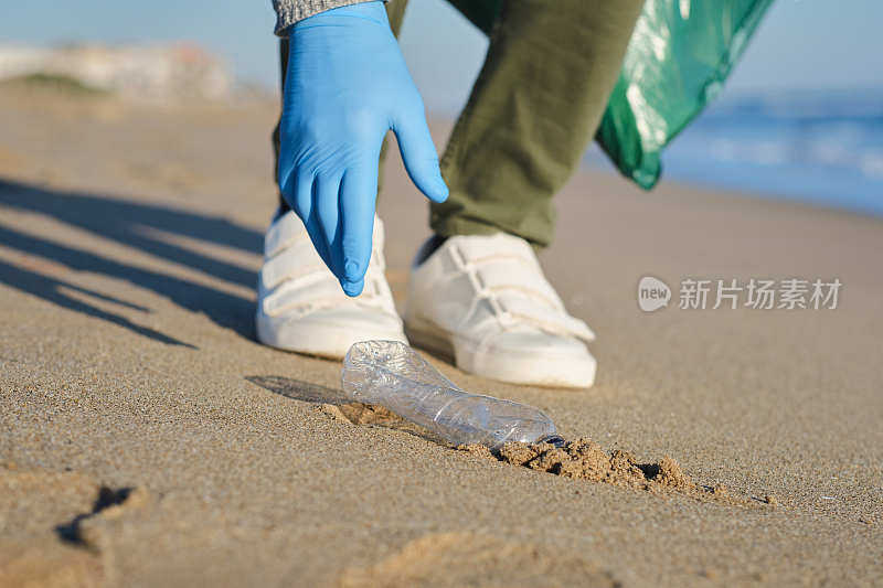 在一个阳光明媚的日子里，地中海海滩上，一个白种人X一代负责收集废物回收的手和一个塑料瓶水的特写镜头