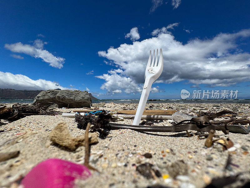 塑料叉污染从沙滩上伸出来，在其他塑料垃圾之间很低