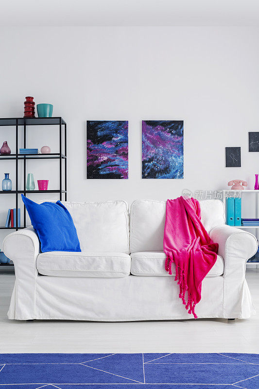 客厅白色沙发上铺着粉色毯子，蓝色地毯和宇宙海报。真实的照片