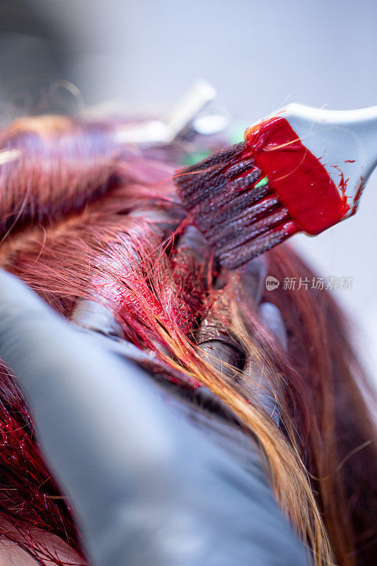 美发师将红色染发剂涂在女人的头发上