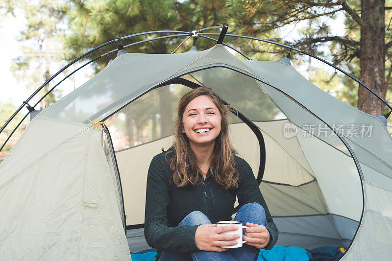 一个年轻女子坐在她的帐篷里，端着一杯咖啡