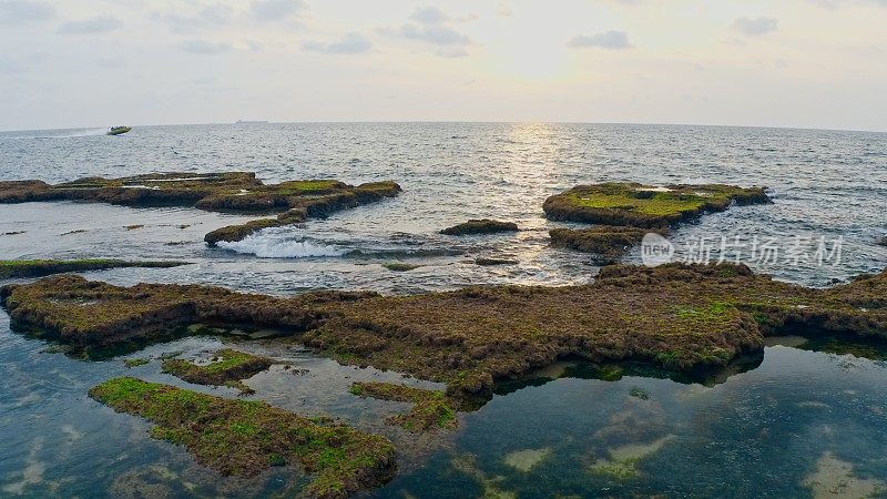 日落时的游船靠近布满苔藓的岩石海岸线