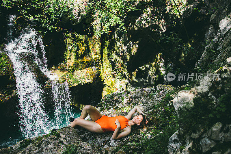 徒步旅行后，穿着泳衣的女人躺在瀑布附近的岩石上