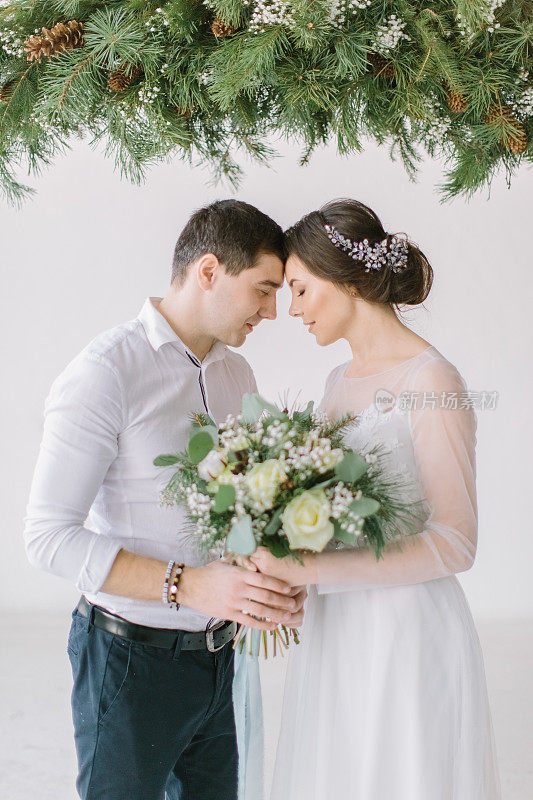 一对年轻夫妇的性感肖像。摄影室婚纱照，装饰松木。新郎和新娘正在寻找婚礼花束