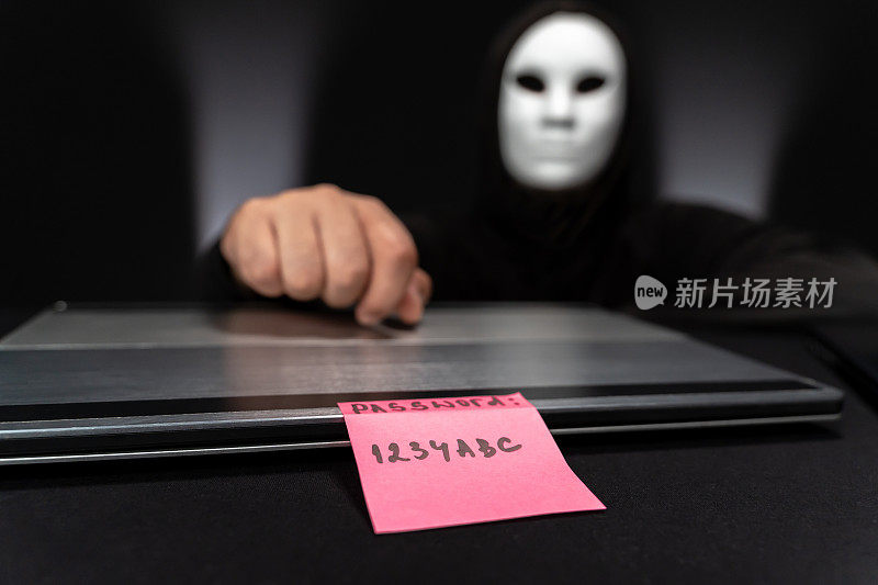带面具的黑客在看带有弱密码的粉色纸条