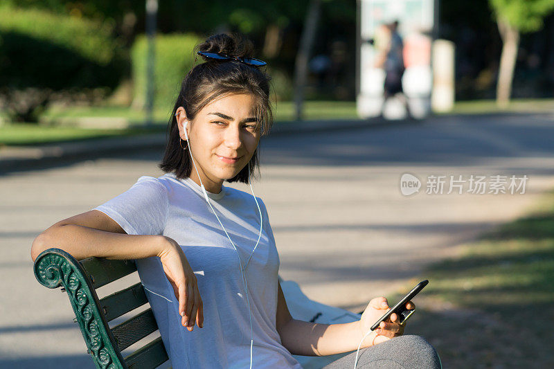 一个穿着运动服的年轻女子正在室外听手机里的音乐