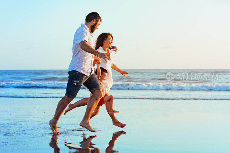家庭-爸爸，妈妈，宝宝在日落海滩上跑步