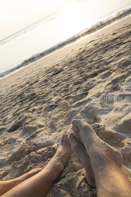 情侣们的脚在白沙滩上放松，日出