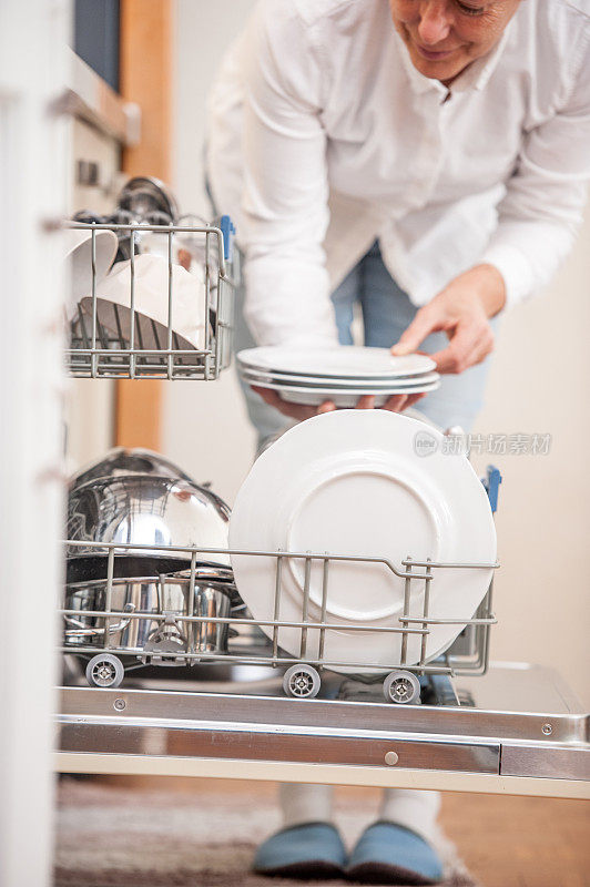 在厨房里从洗碗机里卸载盘子的家庭主妇